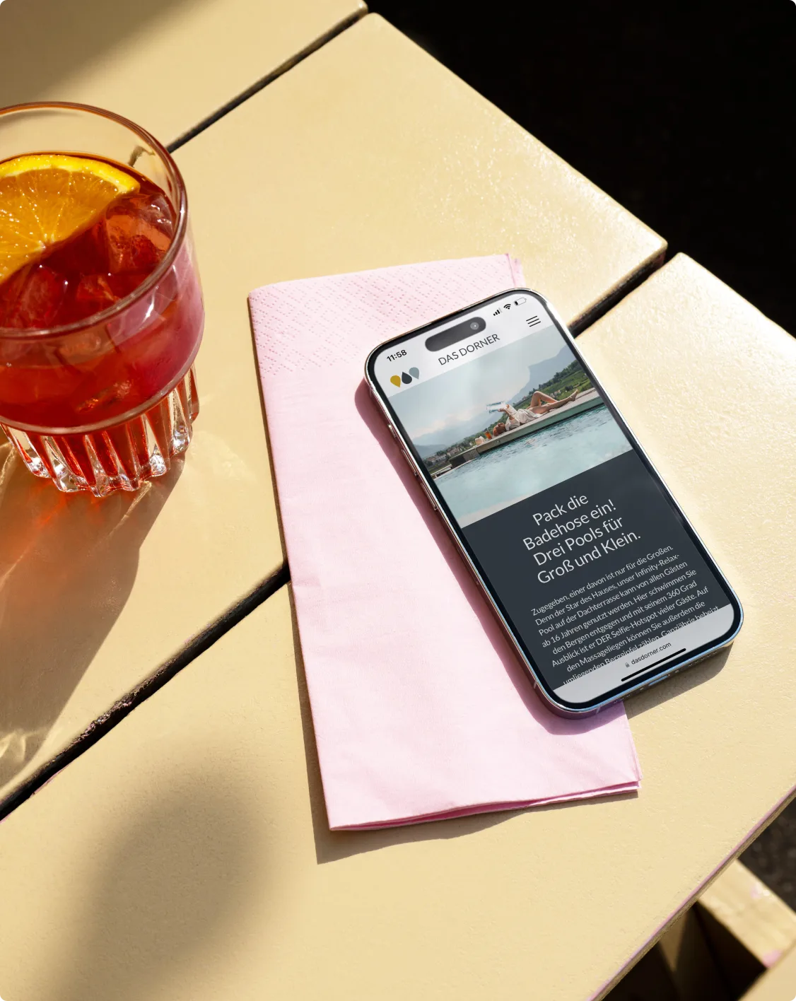 Aperitif mit Orangenscheibe neben dem iPhone mit Pool-Story